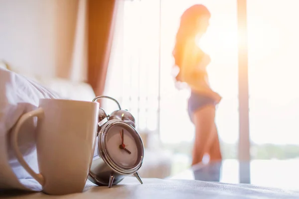 Soft light and Blurred image alarm clock placed next to bed woke up at set time for woman to wake up and prepare to leave for work on time. The idea of setting an alarm using an alarm clock