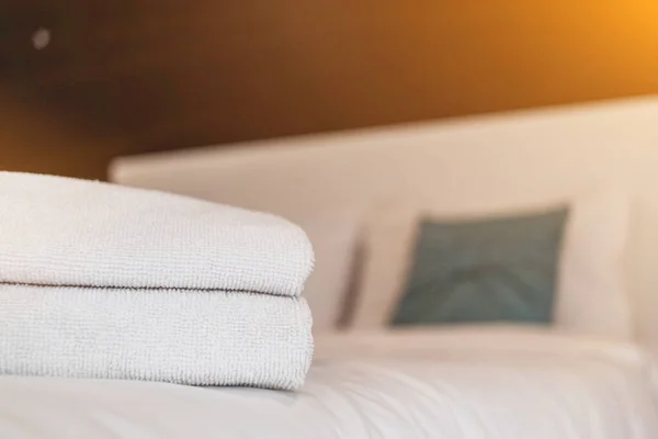 Clean white towels are folded beside bed to be ready for customers to use when it\'s time to take shower because towels are essential for guests to stay. Blurred background with Copy Space for design.