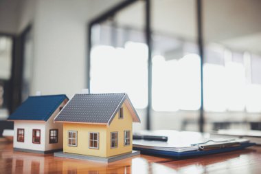 Real estate sales documents and model homes are placed on tables inside real estate sales offices to prepare prospective buyers to sign real estate sales contracts with dealers.