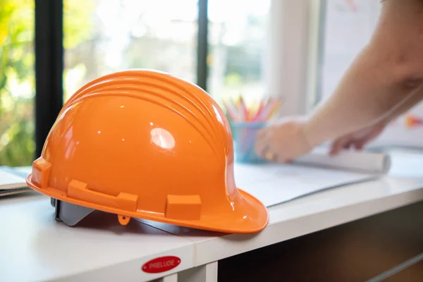 orange hard hats sit on construction engineers desks because hard hats are essential when entering construction site for the safety of engineers.  concept of wearing hard hat to protect head in site.