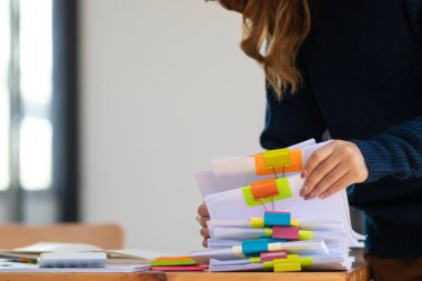 İş kadını elleri, iş adamı ile görüşmede doğru belgeleri kullanmaları için yönetim kuruluna göndermeden önce masaya yığılmış belgeleri aramak ve gözden geçirmek üzere kağıt yığınları üzerinde çalışıyor.