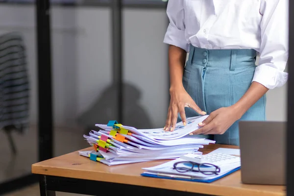 Businesswoman hands working on stacks of paper documents to search and review documents piled on table before sending them to board of directors to use  correct documents in meeting with Businessman