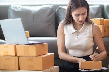 İnternet üzerinden müşteri siparişi paketini kontrol eden kadın, KOBİ 'li bir girişimci olduğu ve internet üzerinden pazarlamak için telefon ve tabletini kullandığı için ev ofisinde yalnızdır. konsept çevrimiçi satış işi