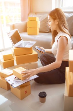 İnternet üzerinden müşteri siparişi paketini kontrol eden kadın, KOBİ 'li bir girişimci olduğu ve internet üzerinden pazarlamak için telefon ve tabletini kullandığı için ev ofisinde yalnızdır. konsept çevrimiçi satış işi