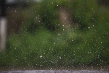 Şiddetli yağmur mevsiminde yere düşen yağmur damlalarının arka planı koyu renk spreyinin bulanık arka planında çok sayıda arsadan su sıçramasına neden olur..