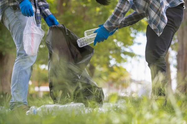 stock image Two man employees use black garbage bags to collect plastic bottles and recyclable waste from the lawn and sidewalks for recycling. Concept of sorting plastic waste for recycling