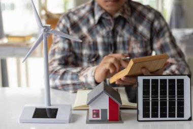 On desk of engineers lay model of house And solar panels to use in planning installation of solar panels to  house in order to get most cost effective energy from installing solar panels. clipart