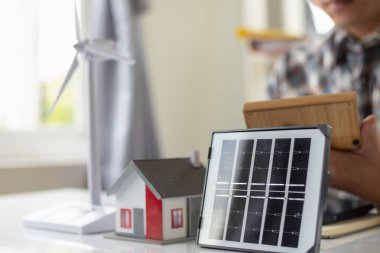 Mühendisler masasında, güneş panellerinin kurulumunu planlamak için güneş panelleri ve ev için kullanılacak ev modelleri ve güneş panelleri vardı..