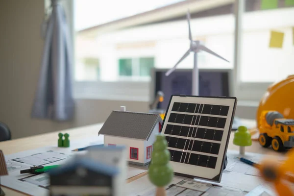 エンジニアの机に太陽電池パネルの設置を計画するのに使用する家および太陽電池パネルのモデルを置いて太陽電池パネルを取付けることからの最も費用効果が大きいエネルギーを得ます — ストック写真
