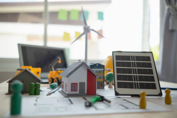 On desk of engineers lay model of house And solar panels to use in planning installation of solar panels to  house in order to get most cost effective energy from installing solar panels.
