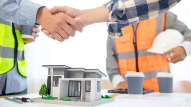 Mimarlar ve inşaat mühendisliği tokalaşmaları sonrasında yapısal planları tartışarak projenin tamamlanmasını hesaplarlar. İnşaat mühendisleri ve mimarlar arasındaki işbirliği ve el sıkışma.