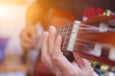 Genç bir adam sahneye çıkmadan önce sahnede gitar çalma hatasını azaltmak için bir müzik çalışma odasında gitar çalma pratiği yapıyor. Yakından Genç Adam pratik için gitar akorları tutuyor..