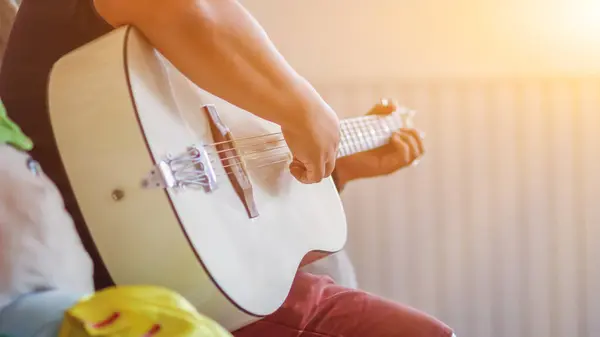 A young man is practicing playing guitar in a music practice room before performing in order to reduce the mistake of playing guitar on stage. Close Up Young man is holding guitar chords for practice.