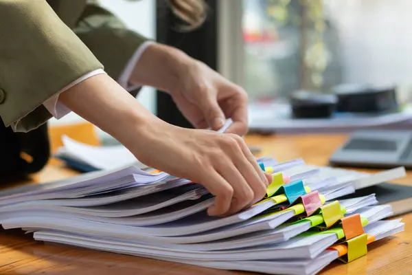 secretary is searching through pile of important documents on office table deliver them to manager for presentation in time at meeting. Concept of difficulty finding information from piles of document