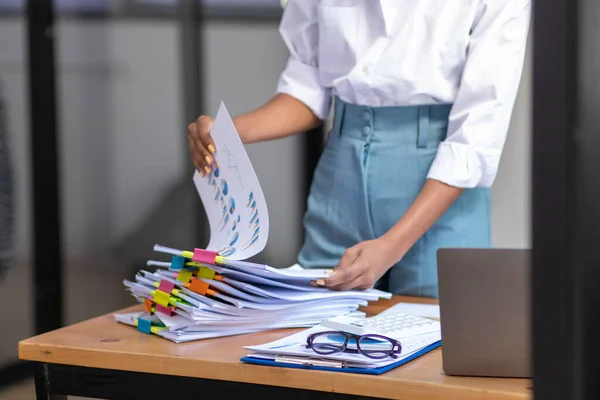 secretary is searching through pile of important documents on office table deliver them to manager for presentation in time at meeting. Concept of difficulty finding information from piles of document