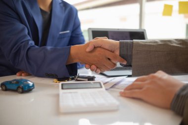 Müşteri ve araba satıcısı, sözleşme imzalamadan ve arabanın anahtarlarını müşteriye teslim etmeden önce satış sözleşmesini kabul ettikten sonra el sıkışıyor. Müşteriler ve araba satıcıları arasında el sıkışma kavramı.