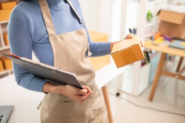 KOBİ işletme operatörü, uygulama çevrimiçi alışverişi ile çevrimiçi pazarlamaya katıldıktan sonra ürünleri almaya gelecek olan teslimat şirketi için ürünleri paket kutusuna koyup teftiş ediyor.