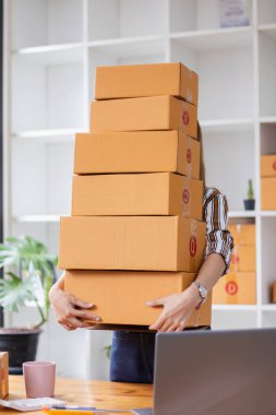 KOBİ işletme operatörü, uygulama çevrimiçi alışverişi ile çevrimiçi pazarlamaya katıldıktan sonra ürünleri almaya gelecek olan teslimat şirketi için ürünleri paket kutusuna koyup teftiş ediyor.