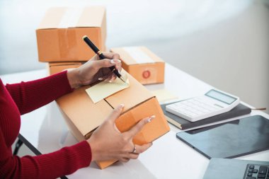 KOBİ işletme operatörü, uygulama çevrimiçi alışverişi ile çevrimiçi pazarlamaya katıldıktan sonra ürünleri almaya gelecek olan teslimat şirketi için ürünleri paket kutusuna koyup teftiş ediyor.