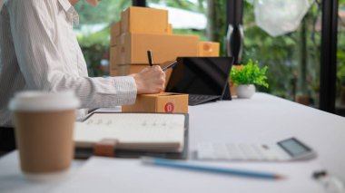 KOBİ işletme operatörü, uygulama çevrimiçi alışverişi ile çevrimiçi pazarlamaya katıldıktan sonra ürünleri almaya gelecek olan teslimat şirketi için ürünleri paket kutusuna koyup teftiş ediyor.
