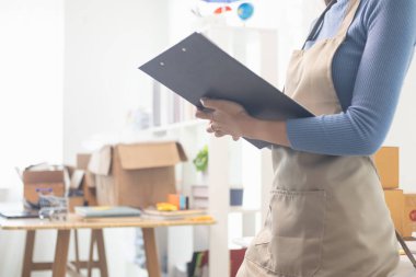 KOBİ işletme operatörü, uygulama çevrimiçi alışverişi ile çevrimiçi pazarlamaya katıldıktan sonra ürünleri almaya gelecek olan teslimat şirketi için ürünleri paket kutusuna koyup teftiş ediyor.