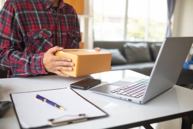 İş adamı, dizüstü bilgisayar ve akıllı telefon kullanarak evde küçük KOBİ işletmelerine yatırım yapmaya karar veriyor ve siparişlere göre ürün paketlemeden önce bir uygulama aracılığıyla online pazarlama yapıyor ve bir şeyler satıyor..