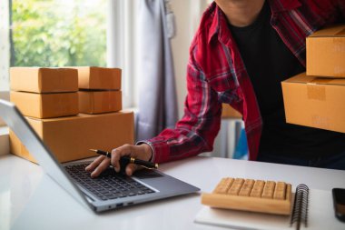 İş adamı, dizüstü bilgisayar ve akıllı telefon kullanarak evde küçük KOBİ işletmelerine yatırım yapmaya karar veriyor ve siparişlere göre ürün paketlemeden önce bir uygulama aracılığıyla online pazarlama yapıyor ve bir şeyler satıyor..