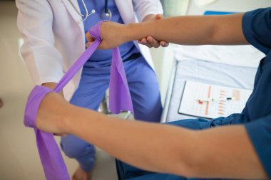 Lastik bant kullanan kadın doktor kas hasarını atlattıktan sonra kas hareketlerinin düzelmesine yardım ediyor ve günlük yaşamını fizik tedavi uygulayarak kullanabilmesini istiyor.