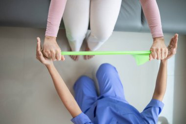 Lastik bant kullanan kadın doktor kas hasarını atlattıktan sonra kas hareketlerinin düzelmesine yardım ediyor ve günlük yaşamını fizik tedavi uygulayarak kullanabilmesini istiyor.