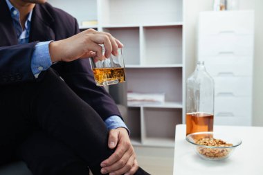 İş adamı, iş hayatında sorunlar yaşadıktan sonra stres atmak için elinde içki bardağıyla oturur. Alkol alan işadamı, başarısız iş girişiminin stresinden kurtuldu.