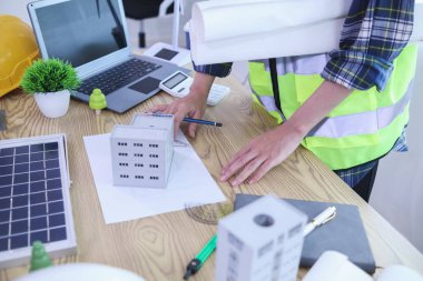 Mühendisler, güneş panelleri ve rüzgar türbinlerini güneş pillerinden gelen yeşil enerji kavramını kullanarak verimli bir şekilde elektrik üretmek üzere binaya yerleştirmeye hazırlanmak için mimarların planlarını gözden geçiriyorlar.