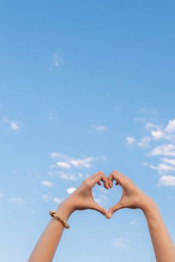 Bir kadın, parlak sabah gökyüzünün arka planına bir kalp sembolü yapmak için elini başının üstüne kaldırır. Çünkü kalp sembolü birbirine karşı sevgi, dostluk ve şefkati simgeler..