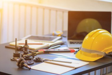 Mühendislik ekibinin ekipmanları ve belgeleri ofisteki masaların üzerinde, güvenlik için bölgeye girerken giyilmek üzere hazırlanmış sarı kasklar da var..