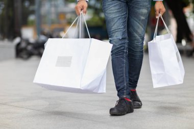 Alışveriş merkezinin içinde alışveriş poşeti tutan işadamı, tatillerde alışveriş yaptıktan sonra mutlu oluyor. İçinde bir sürü ürün bulunan kese kağıdı iş adamının elinde..