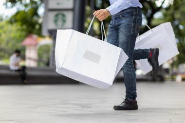 Alışveriş merkezinin içinde alışveriş poşeti tutan işadamı, tatillerde alışveriş yaptıktan sonra mutlu oluyor. İçinde bir sürü ürün bulunan kese kağıdı iş adamının elinde..