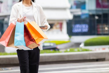 Alışveriş merkezinde alışveriş poşetleri tutan Asyalı bir kadın ve festival boyunca alışveriş yaptıktan sonra mutlu. İçinde pek çok ürünün bulunduğu kağıt torbalar Asyalı kadının elinde..