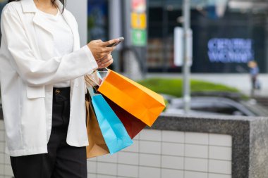 Alışveriş merkezinde alışveriş poşetleri tutan Asyalı bir kadın ve festival boyunca alışveriş yaptıktan sonra mutlu. İçinde pek çok ürünün bulunduğu kağıt torbalar Asyalı kadının elinde..