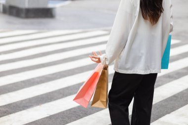 Alışveriş merkezinde alışveriş poşetleri tutan Asyalı bir kadın ve festival boyunca alışveriş yaptıktan sonra mutlu. İçinde pek çok ürünün bulunduğu kağıt torbalar Asyalı kadının elinde..
