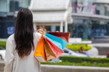 Bir alışveriş merkezinde alışveriş poşetleri tutan iş kadını, festival sırasında ihtiyaçlarını karşıladığı için mutlu. İçinde bir sürü ürün bulunan kağıt torbalar Asyalı iş kadınının elinde..