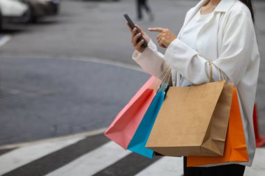 Alışveriş merkezinde alışveriş poşetleri tutan Asyalı bir kadın ve festival boyunca alışveriş yaptıktan sonra mutlu. İçinde pek çok ürünün bulunduğu kağıt torbalar Asyalı kadının elinde..