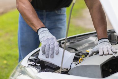 Tamirci, motor soğutma kapasitesini arttırmak için arabayı kontrol ediyor ve radyatöre su ekliyor. Servis merkezi başvurusundan aranan tamirci müşteriye yardım ediyor