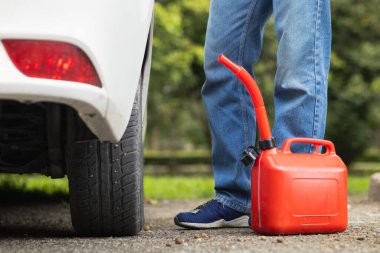 young man holds red gallon of gasoline which is reserve gasoline for emergency use when running out of fuel during trip or using reserve gasoline in red gallon to help people who run out of fuel. clipart