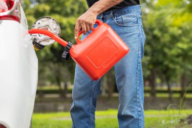 Delikanlının elinde kırmızı bir galon benzin var. Yolculuk sırasında yakıtı biterken ya da benzini biterken kullanılması için kırmızı bir galon benzin..