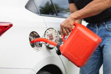 Delikanlının elinde kırmızı bir galon benzin var. Yolculuk sırasında yakıtı biterken ya da benzini biterken kullanılması için kırmızı bir galon benzin..