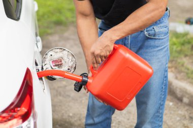 young man holds red gallon of gasoline which is reserve gasoline for emergency use when running out of fuel during trip or using reserve gasoline in red gallon to help people who run out of fuel. clipart