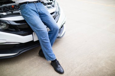 Delikanlı motor sorunu olan bir arabanın kaputunun önünde duruyor ve cep telefonuyla yerel bir araba servisini arıyor ve tamirciye gelip arabayı kontrol etmesini bildiriyor..
