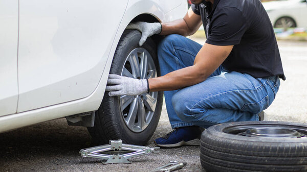 Механик готовит оборудование и запасное колесо для замены шины автомобиля, у которого спустило колесо во время поездки, и механик был вызван экстренным приложением сервисного центра.