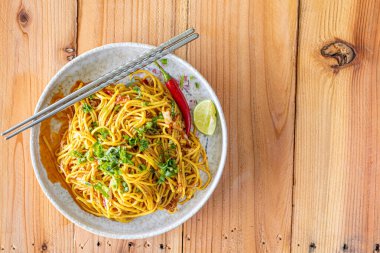 Tabakta servis edilen Khao Soi Yuan Naan, baharatlı ve susamlı baharatlı domuz pirzolası ve kişniş ile karıştırılmış Khao Soi eriştesidir. Erişte Çin yemeği Tai Yai yemeği