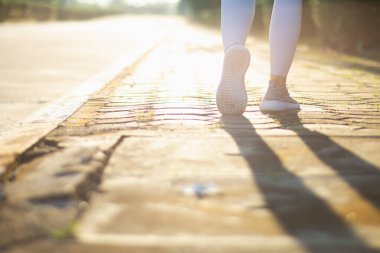 Spor kıyafeti giyen ve spor ayakkabısı giyen genç bir kadın gideceği yere giden yolda yürüyor. Genç bir kadın iki ayağıyla hedefine doğru kararlı bir şekilde yürüyor..