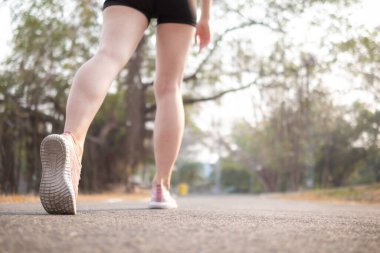 Spor kıyafeti giyen ve spor ayakkabısı giyen genç bir kadın gideceği yere giden yolda yürüyor. Genç bir kadın iki ayağıyla hedefine doğru kararlı bir şekilde yürüyor..